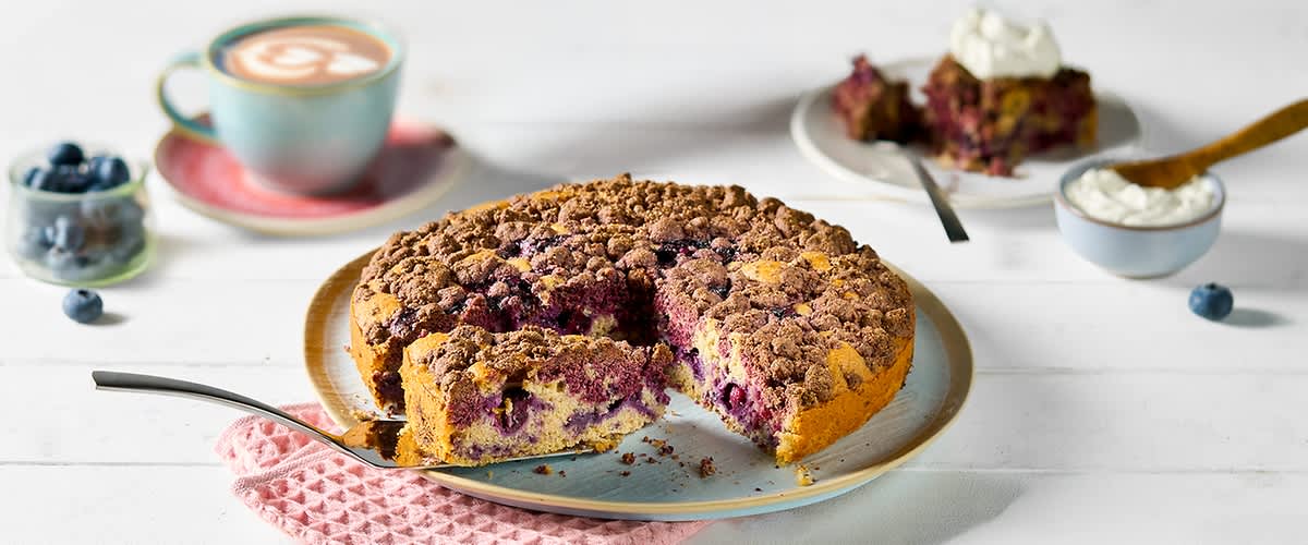 Torta di mirtilli con crumble su tavolo bianco con tazza di cappuccino in secondo piano