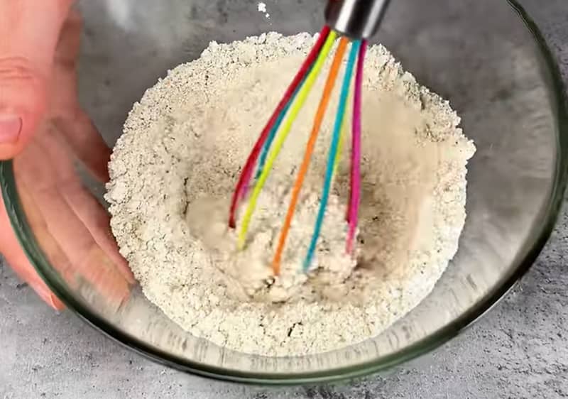 Frusta colorata mescola farina in una ciotola di vetro