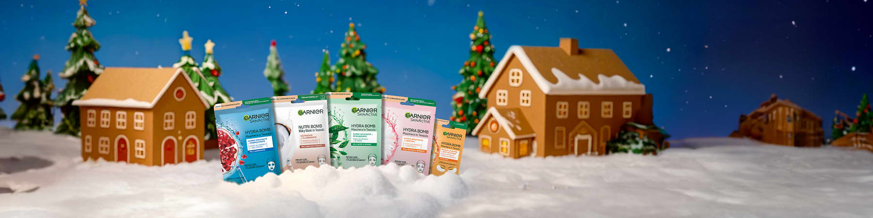 Maschere viso Garnier su neve con case natalizie sullo sfondo