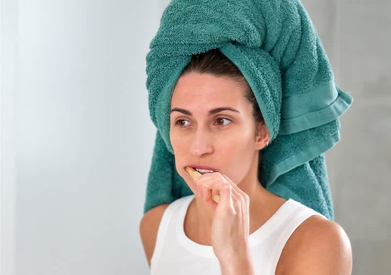 Donna con asciugamano verde avvolto sulla testa che lava i denti