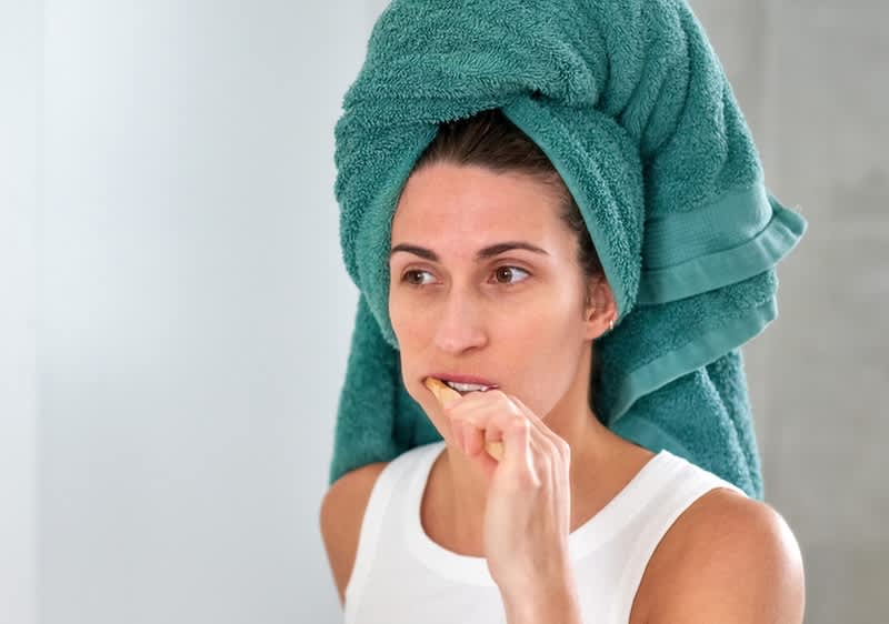 Donna con asciugamano verde avvolto sulla testa che lava i denti