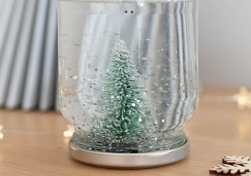 Albero di Natale in una palla di vetro con neve finta su tavolo di legno