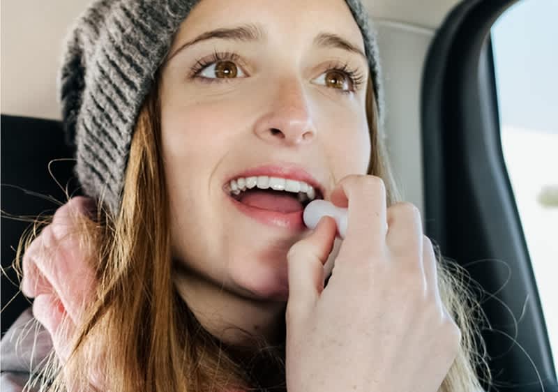 Donna giovane con abbigliamento invernale si applica burrocacao sulle labbra mentre è in macchina