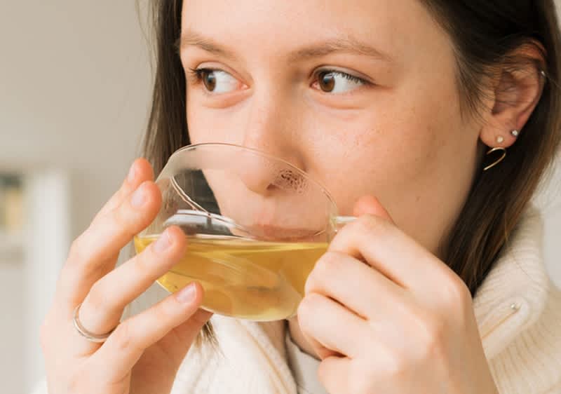 Donna castana con maglione bianco sorseggia tazza di tè caldo