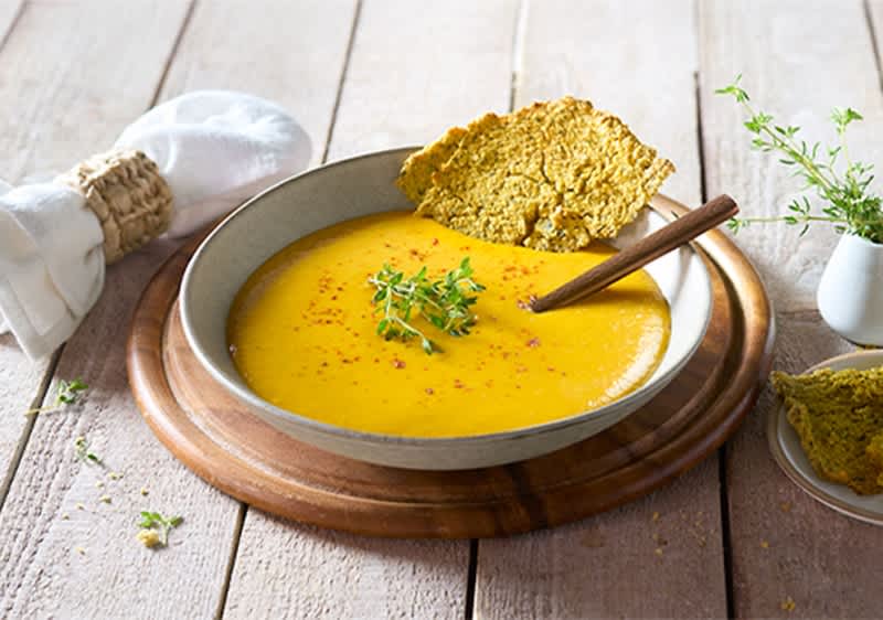 Piatto con vellutata di zucca con cracker e erbe su tavola di legno