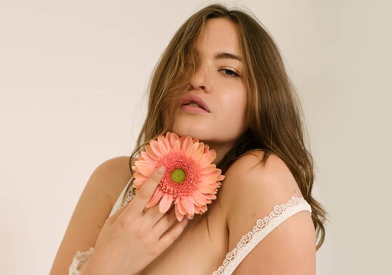 Una donna tiene un fiore rosa vicino alla spalla, indossando un indumento con pizzo.