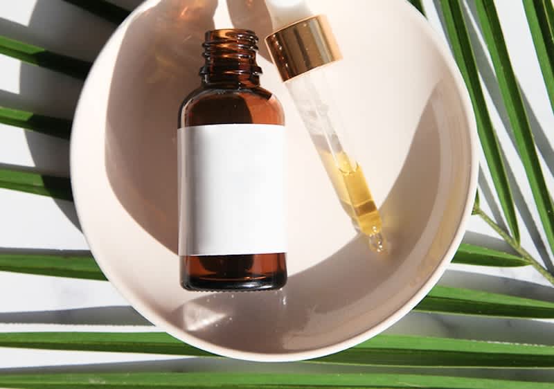 Boccetta di olio di ricino e contagocce su piatto con foglia verde