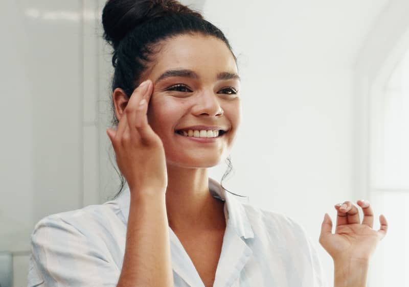 Una ragazza in pigiama si guarda allo specchio sorridendo. 
