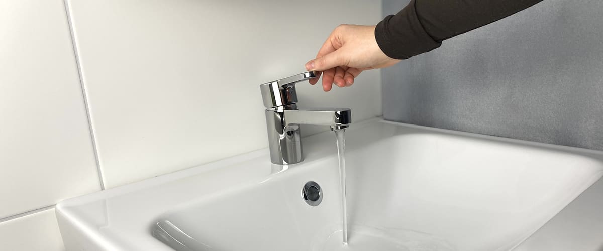Una mano apre il rubinetto di un lavandino bianco. 