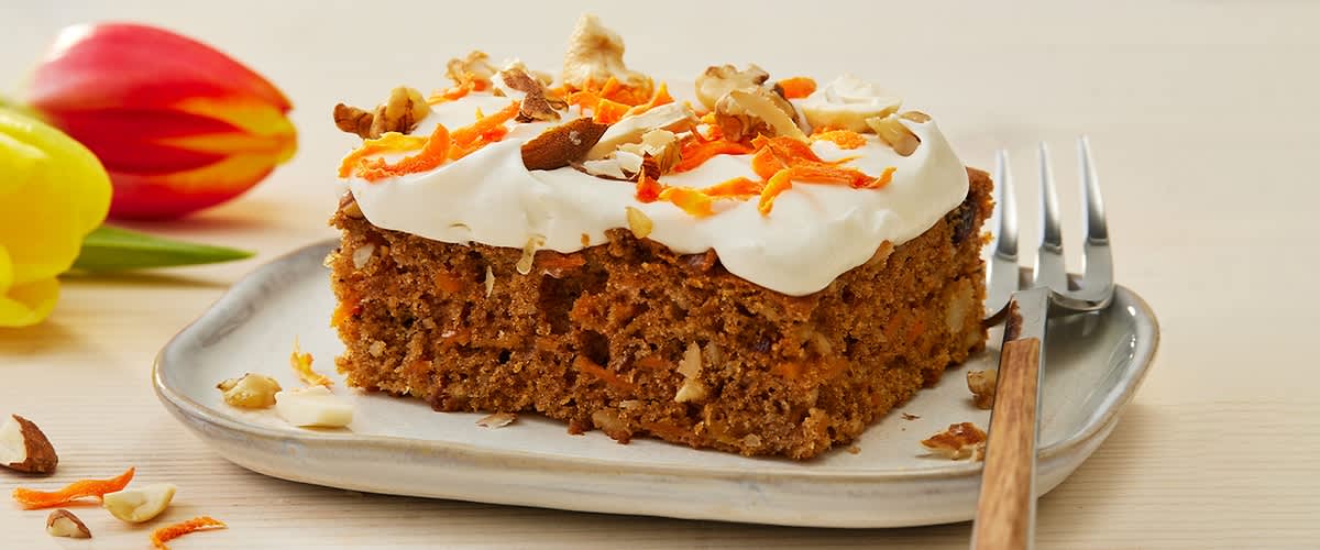 Fetta di torta di carote vegana in teglia su un piatto con una forchetta.