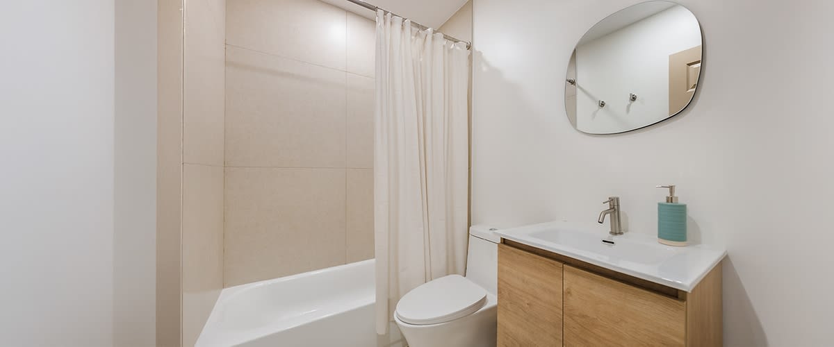 Un moderno bagno con una vasca da bagno bianca, una tenda da doccia beige, un lavandino bianco e uno specchio ovale.