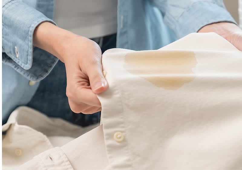 Persona tiene in mano una camicia bianca con una macchia di grasso