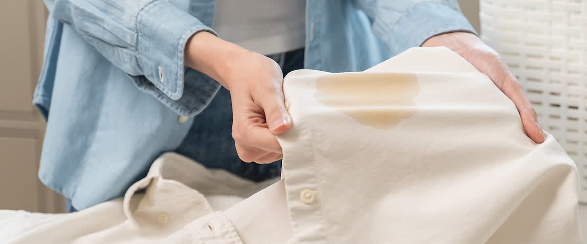 Persona tiene in mano una camicia bianca con una macchia di grasso