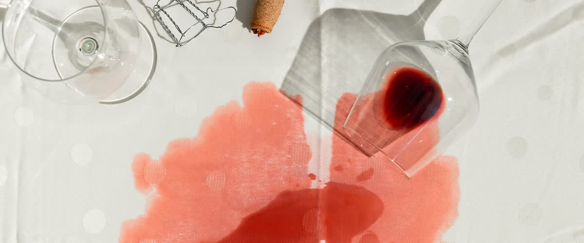 Vino versato su tovaglia bianca con bicchiere rovesciato e tappo