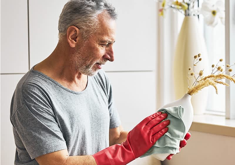 Uomo di mezza età con guanti rossi da cucina che pulisce un vaso.