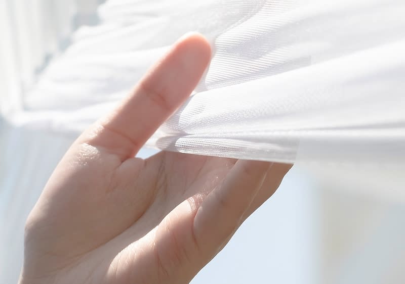 Mano che solleva una tenda bianca leggera alla finestra