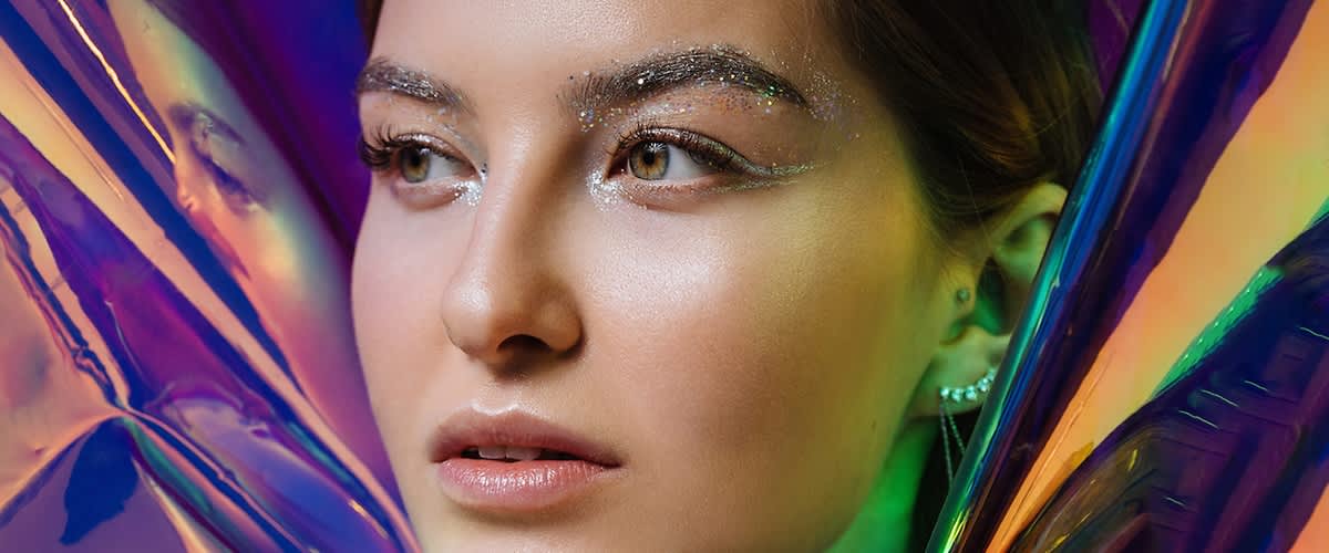 Donna con trucco glitterato su sfondo viola e verde.