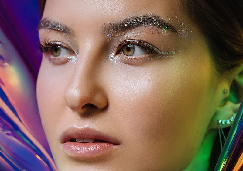 Donna con trucco glitterato su sfondo viola e verde.