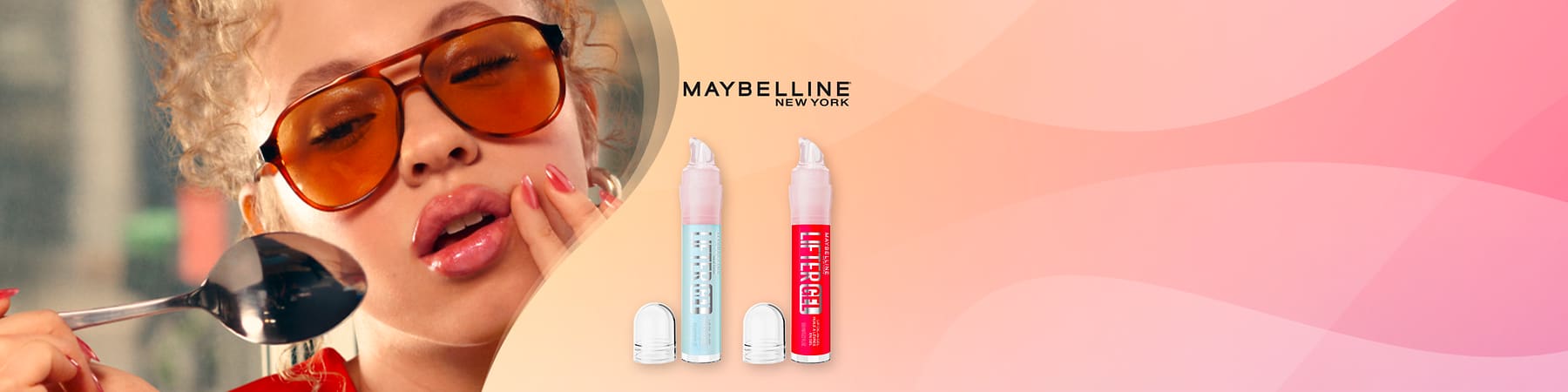 Maybelline donna con occhiali arancioni e due prodotti per labbra su sfondo rosa