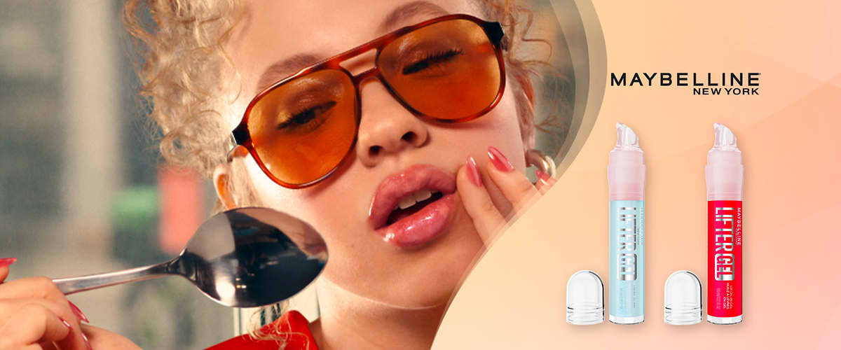Maybelline donna con occhiali arancioni e due prodotti per labbra su sfondo rosa