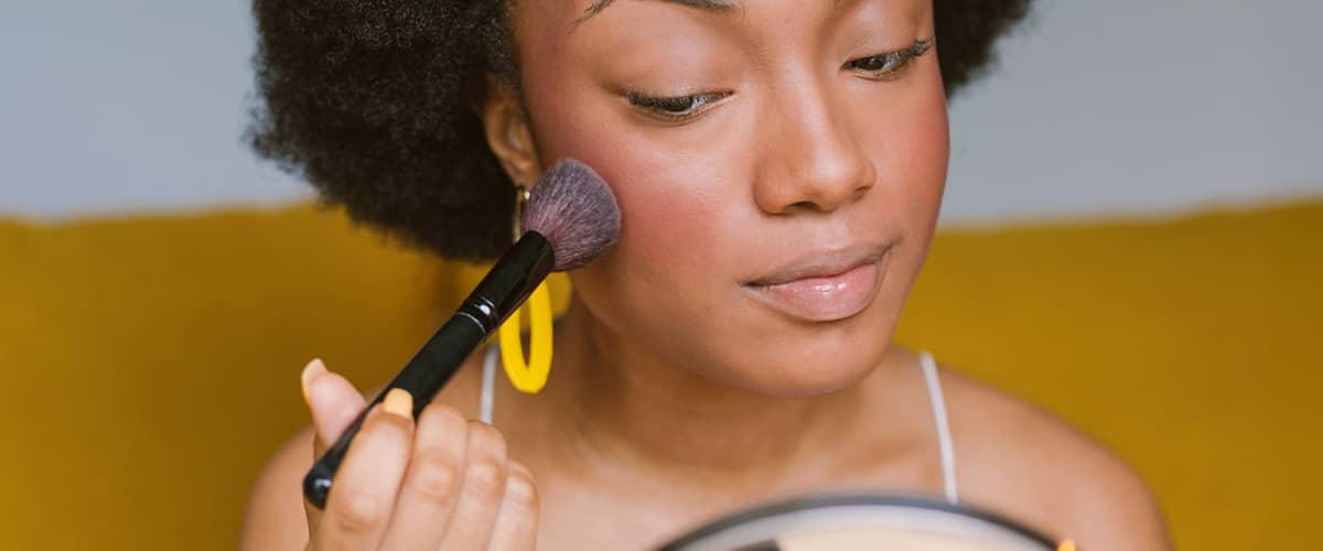 Donna che applica blush sulle guance con pennello davanti a uno specchio