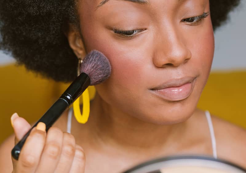 Donna che si applica blush sulle guance con pennello davanti a uno specchio
