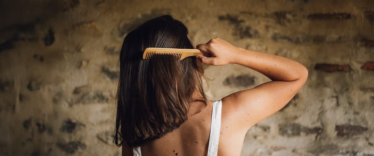 Donna di spalle che si pettina i capelli con un pettine in legno