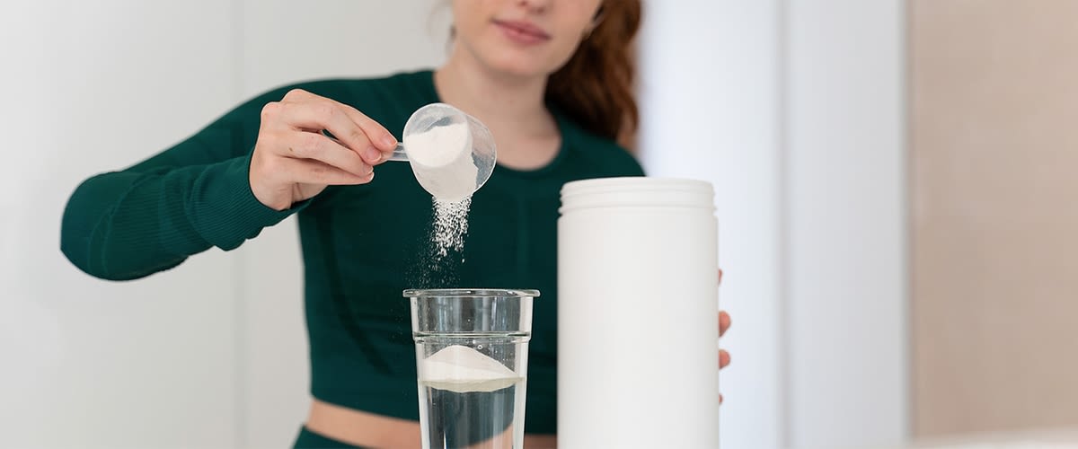 Donna versa aroma in polvere in bicchiere d'acqua accanto al barattolo