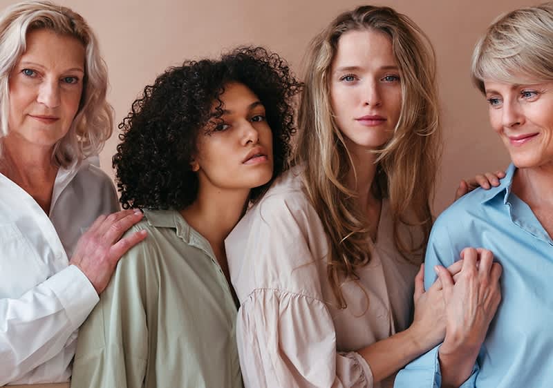 Quattro donne di diverse età in posa ravvicinata vestite in camicie neutre
