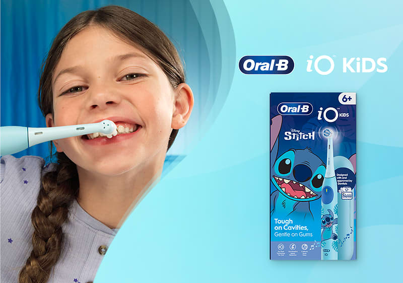 Bambina sorridente che si spazzola i denti con uno spazzolino elettrico Oral‑B iO Kids.