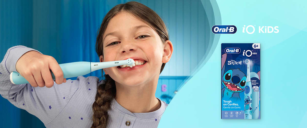 Bambina sorridente che si spazzola i denti con uno spazzolino elettrico Oral‑B iO Kids.