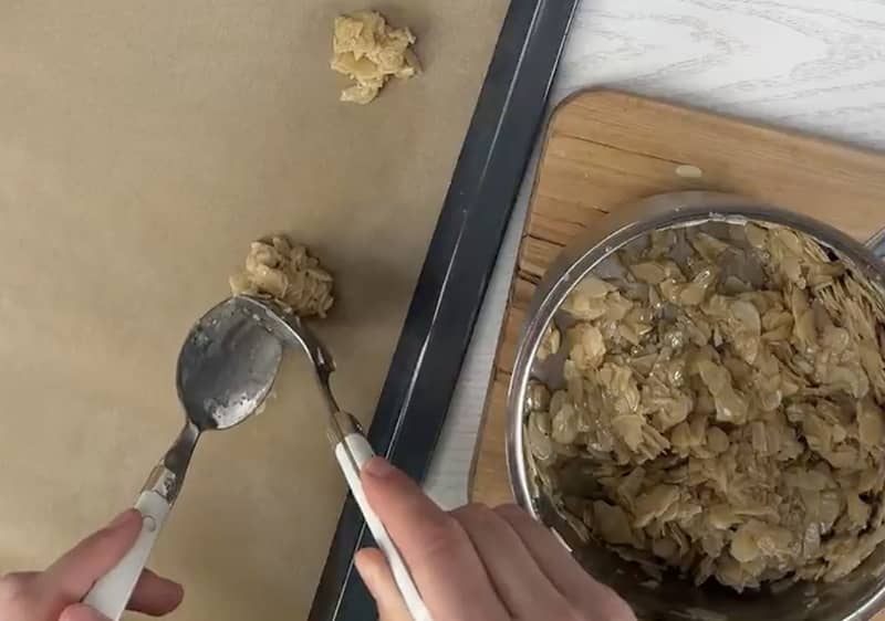 Due cucchiai versano porzioni di impasto dei florentines su una teglia foderata di carta forno.