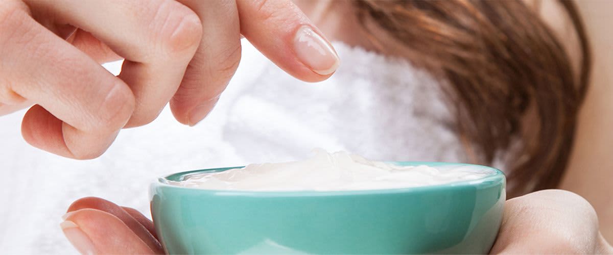 Kobieta w ręczniku trzyma palec nad turkusową miską z jogurtem