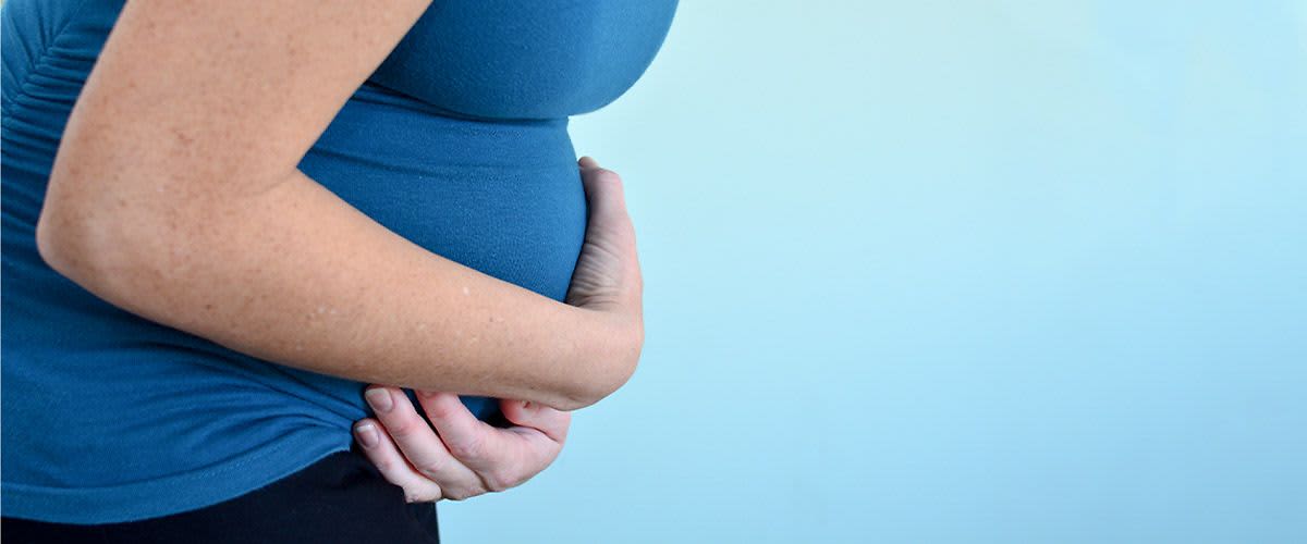 Ciężarna kobieta w trakcie skurczu trzyma się za brzuch z powodu bólu