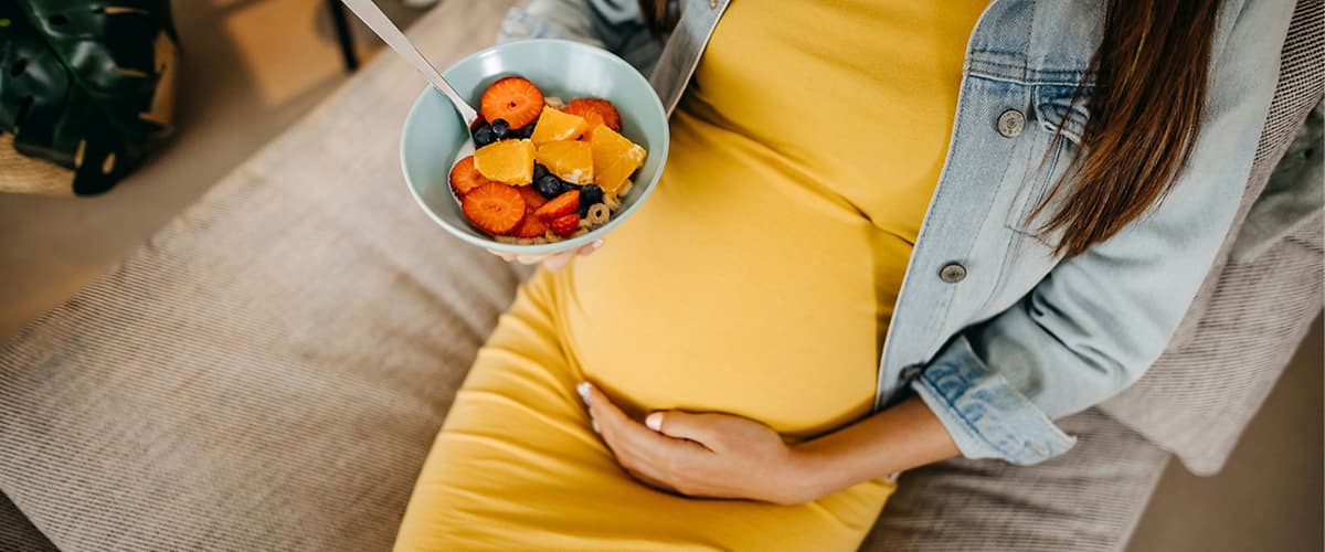 Kobieta w ciąży z miską pełną owoców