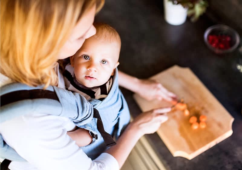 Kobieta z dzieckiem w nosidle kroi warzywa