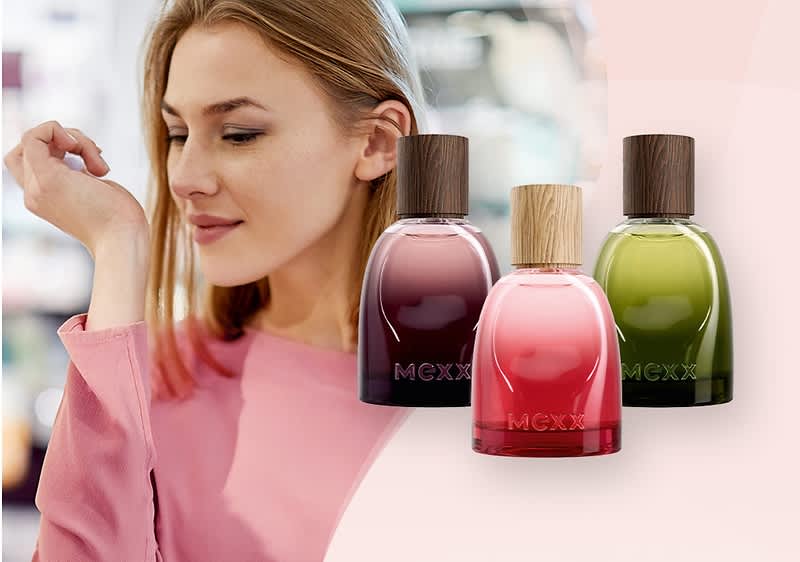 Kobieta sprawdzająca perfumy, po prawej stronie na jasnoróżowym tle trzy perfumy MEXX: Inspired Warmth woda perfumowana męska, Inspired Nature woda perfumowana męska oraz Inspired Nature woda perfumowana damska