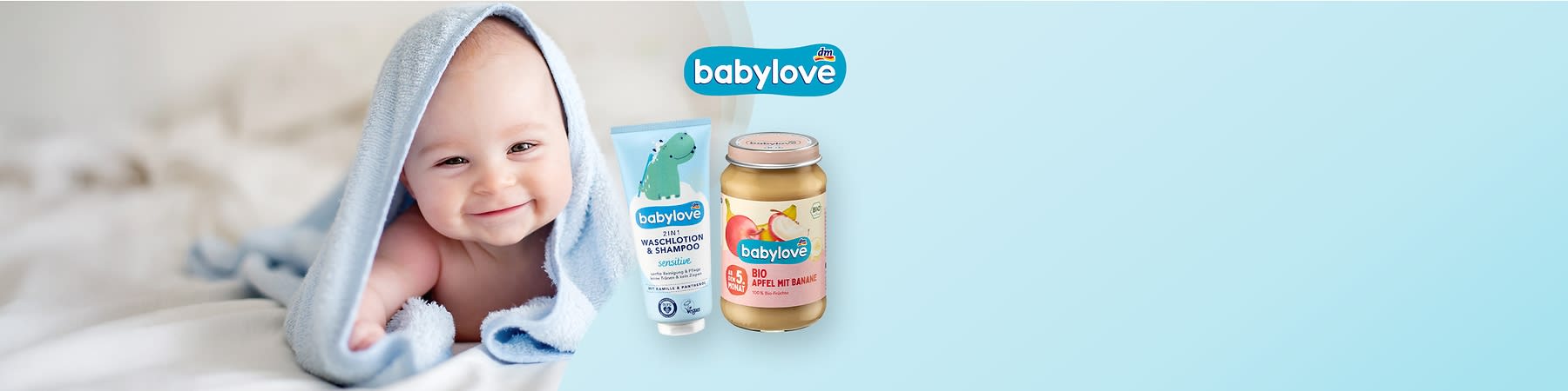 Niemowlę owinięte w niebieski ręcznik leżące na białym kocu obok słoiczka jedzenia dla niemowląt marki babylove i szamponu.