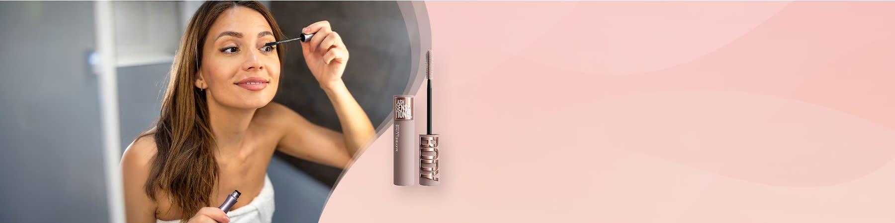 Kobieta nakłada tusz do rzęs przed lustrem, obok widoczna maskara Maybelline New York.