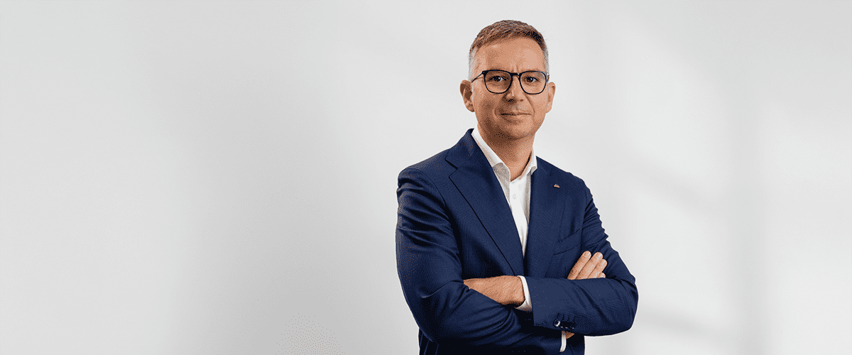 Bărbat în costum albastru cu brațele încrucișate pe fundal alb