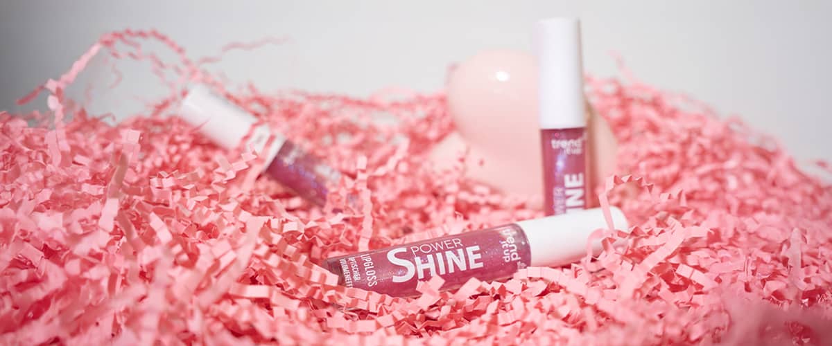 Trei tuburi de gloss de buze roz pe hârtie decorativă roz