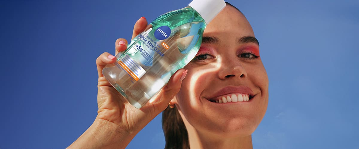 O mână ținând o sticlă de loțiune de curățare Nivea sub cer albastru