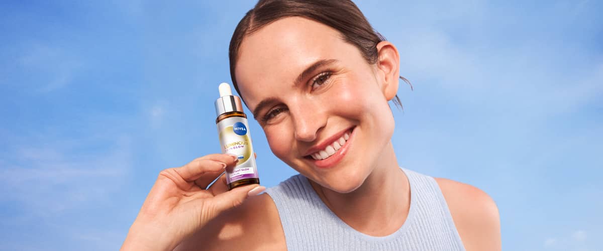 Persoană ținând un ser facial în mână pe fundal albastru