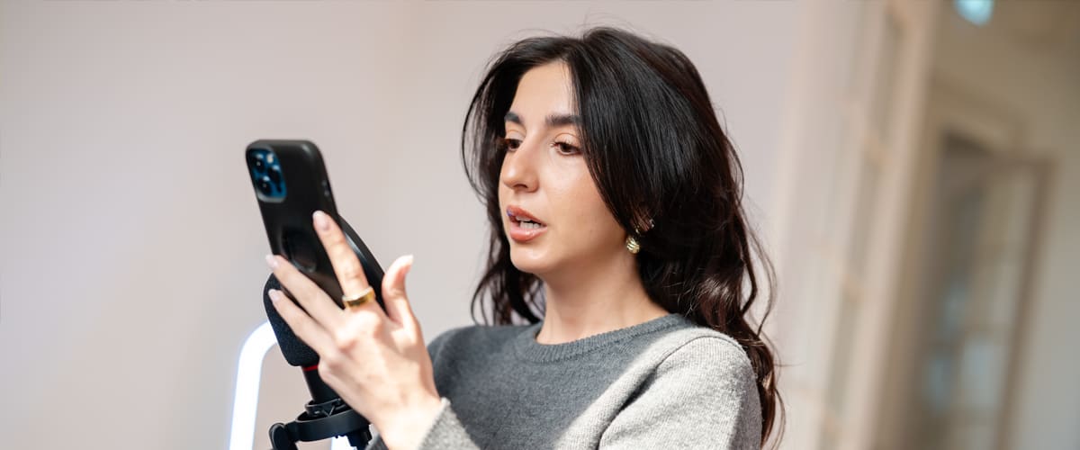 Influencer tânără făcând selfie cu telefonul pe trepied în interior