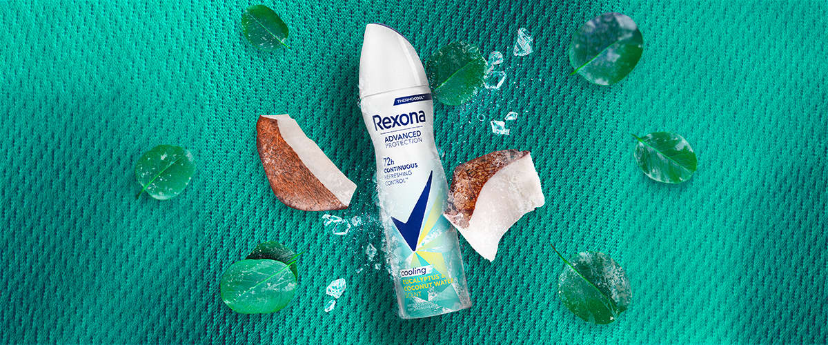 Deodorant spray Rexona pe fundal verde cu bucăți de nucă de cocos și frunze verzi