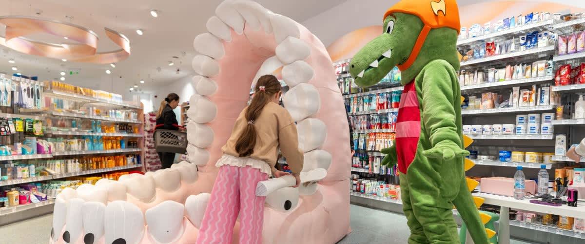Copil în magazin care explorează o machetă uriașă de dinți în fața unei mascote de crocodil