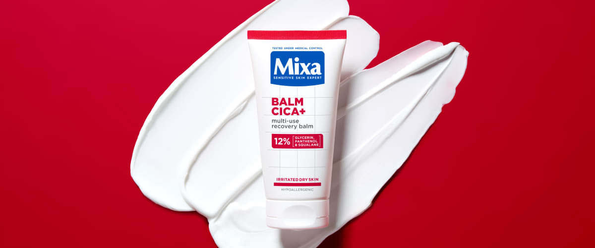 Balsam Mixa Cica+ tub așezat pe cremă albă pe fundal roșu