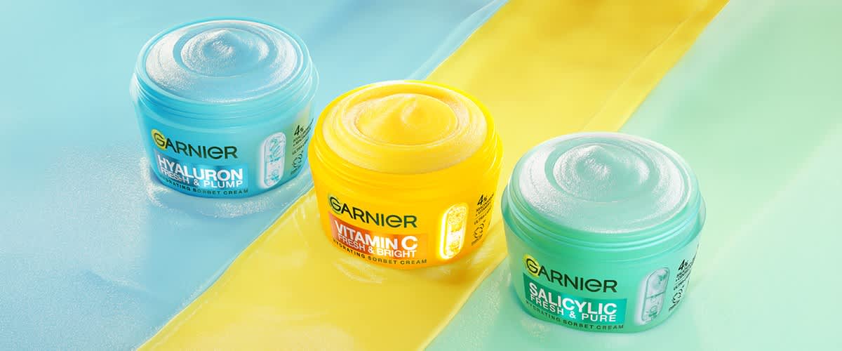 cremă de față Garnier în borcane colorate galben și verde pe fundal albastru și galben