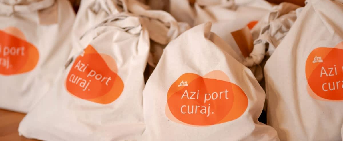 Sacoșe din pânză cu etichetă portocalie Azi port curaj aranjate pe masă