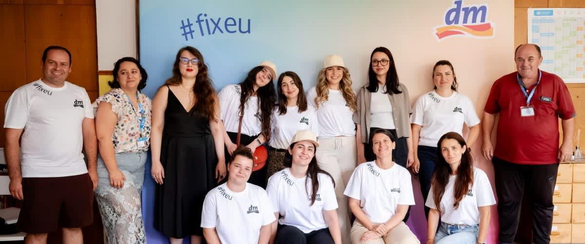 Echipă de voluntari zâmbind în fața unui banner cu logo dm și textul #fixeu